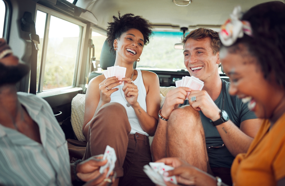 Friends, car road trip and game of card for diversity group of people bond and enjoy quality vacation time together. Transport travel, freedom smile and happy gen z students play fun match on holiday
